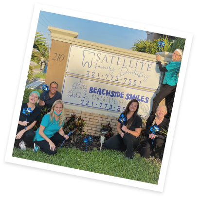 Dental team standing next to outdoor sign for Beachside Smiles Pediatric Dentistry