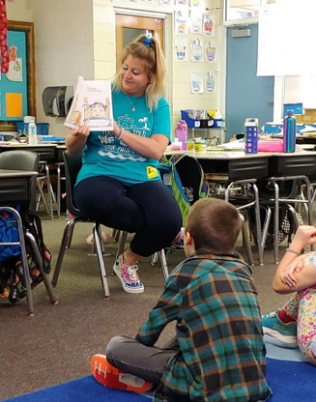 Pediatric dental team member reading a picture book to a classroom of kids