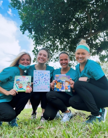 Four dental team members smiling outdoors with picture books