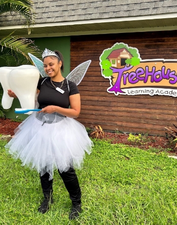 Dental team member dressed as tooth fairy and holding large model of a tooth