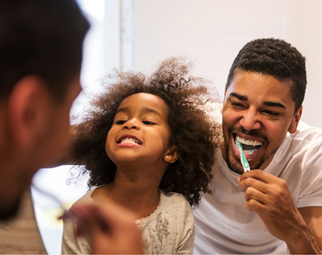 Father and young daughter brushing their teeth together