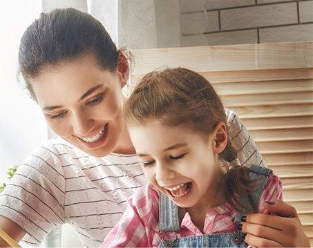 Girl in overalls smiling at table with her mother