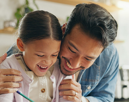 Father hugging his daughter and watching her draw