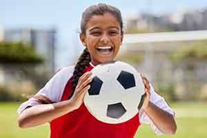 Young girl smiling while holding soccer ball on field